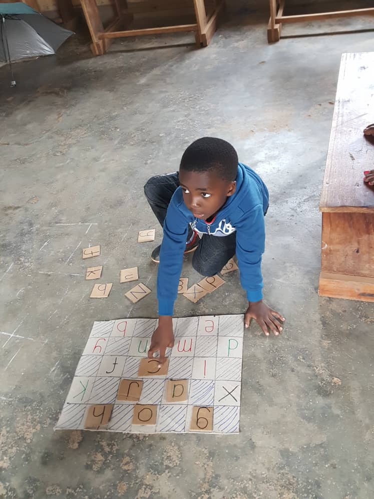 A boy matching letter tiles to a handmade alphabet grid